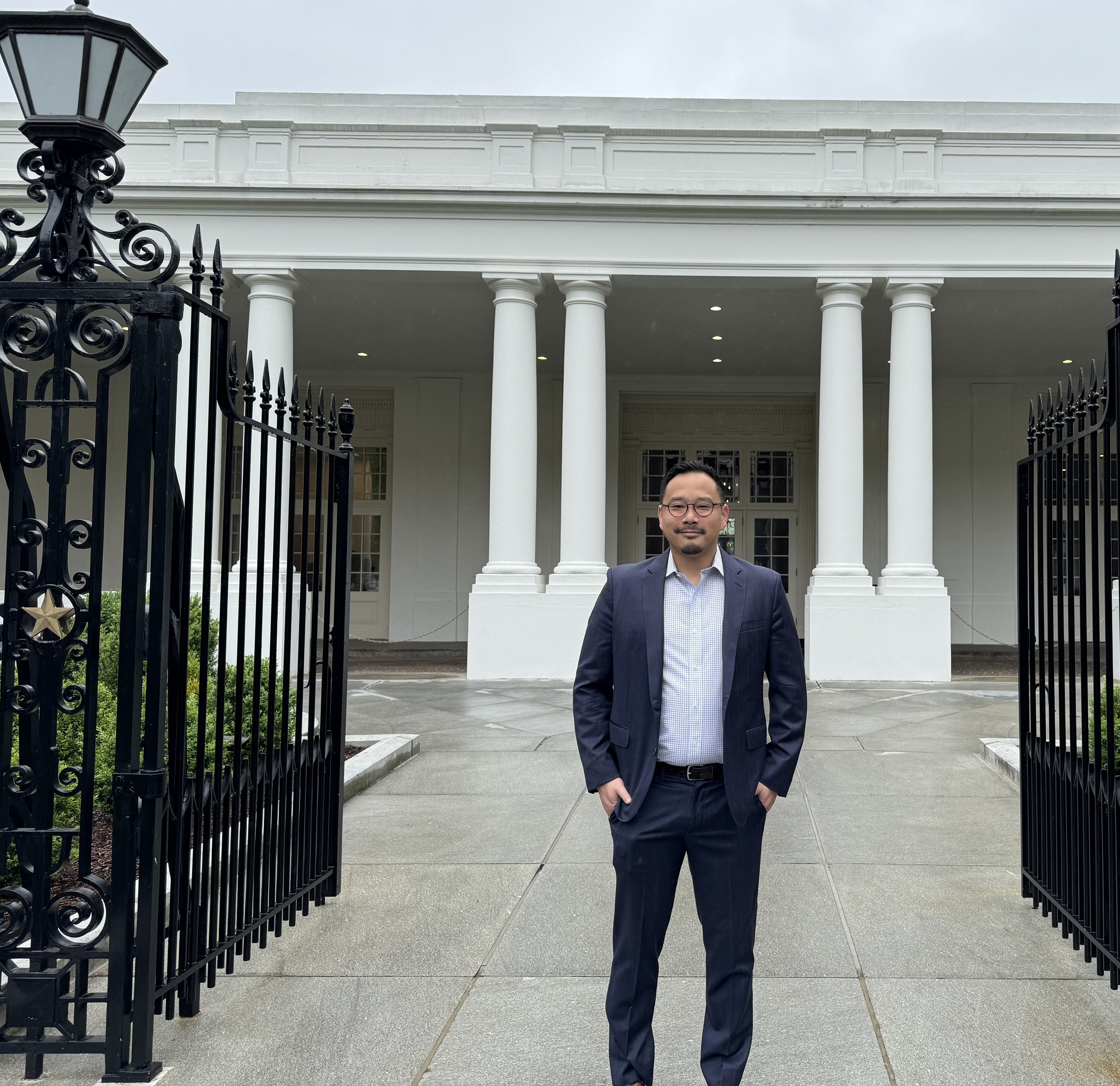 Dr. Charles Lu standing in a navy suit at the West Wing colonnade entrance